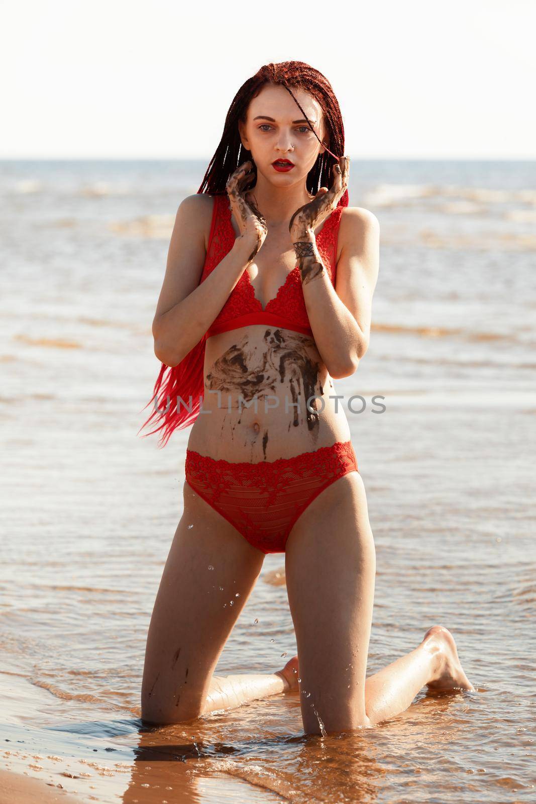 Beautiful girl outdoors enjoying nature. Seminude girl with scarlet dreadlocks in a red bathing suit sunbathes on the beach