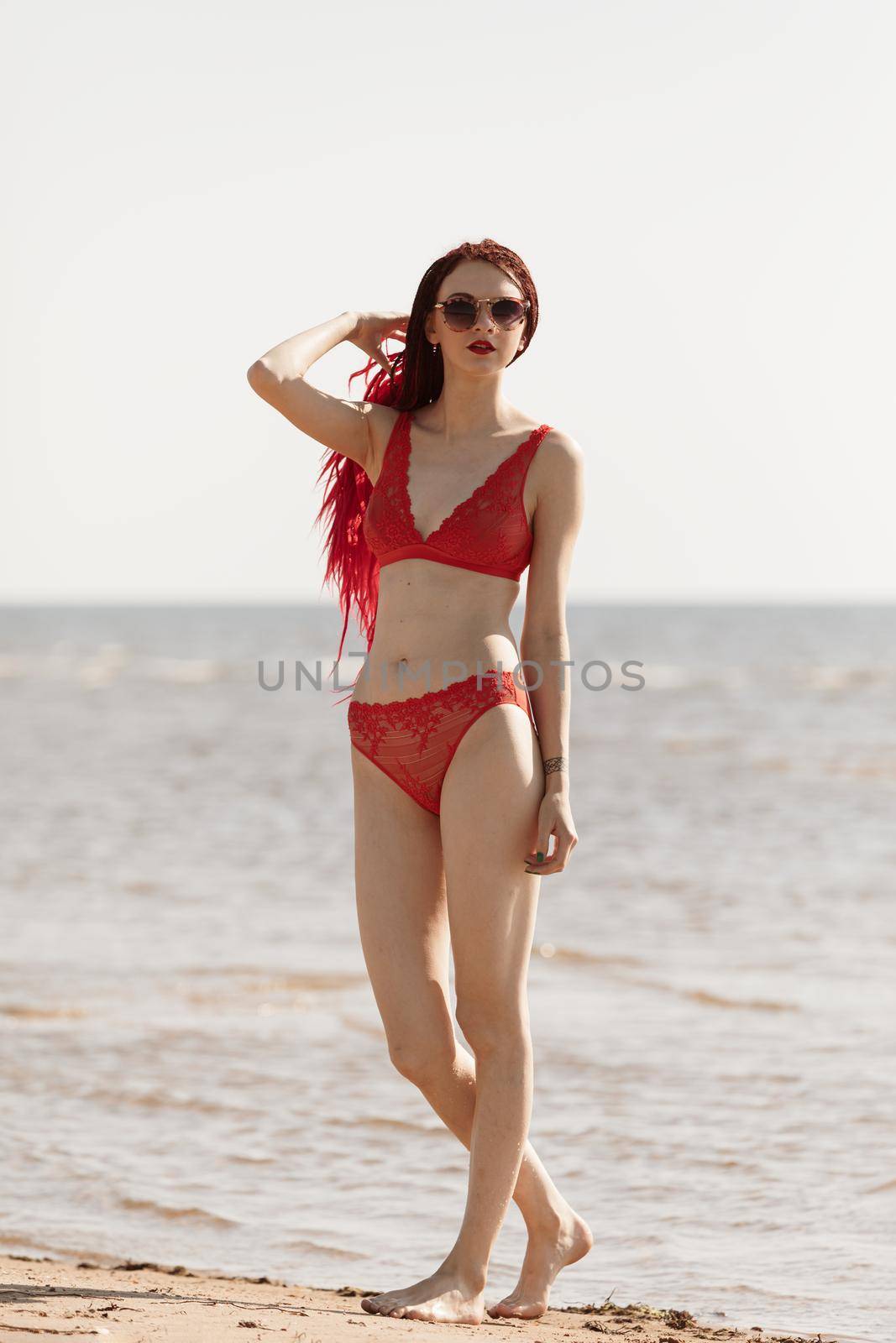 Beautiful girl outdoors enjoying nature. Seminude girl with scarlet dreadlocks in a red bathing suit sunbathes on the beach