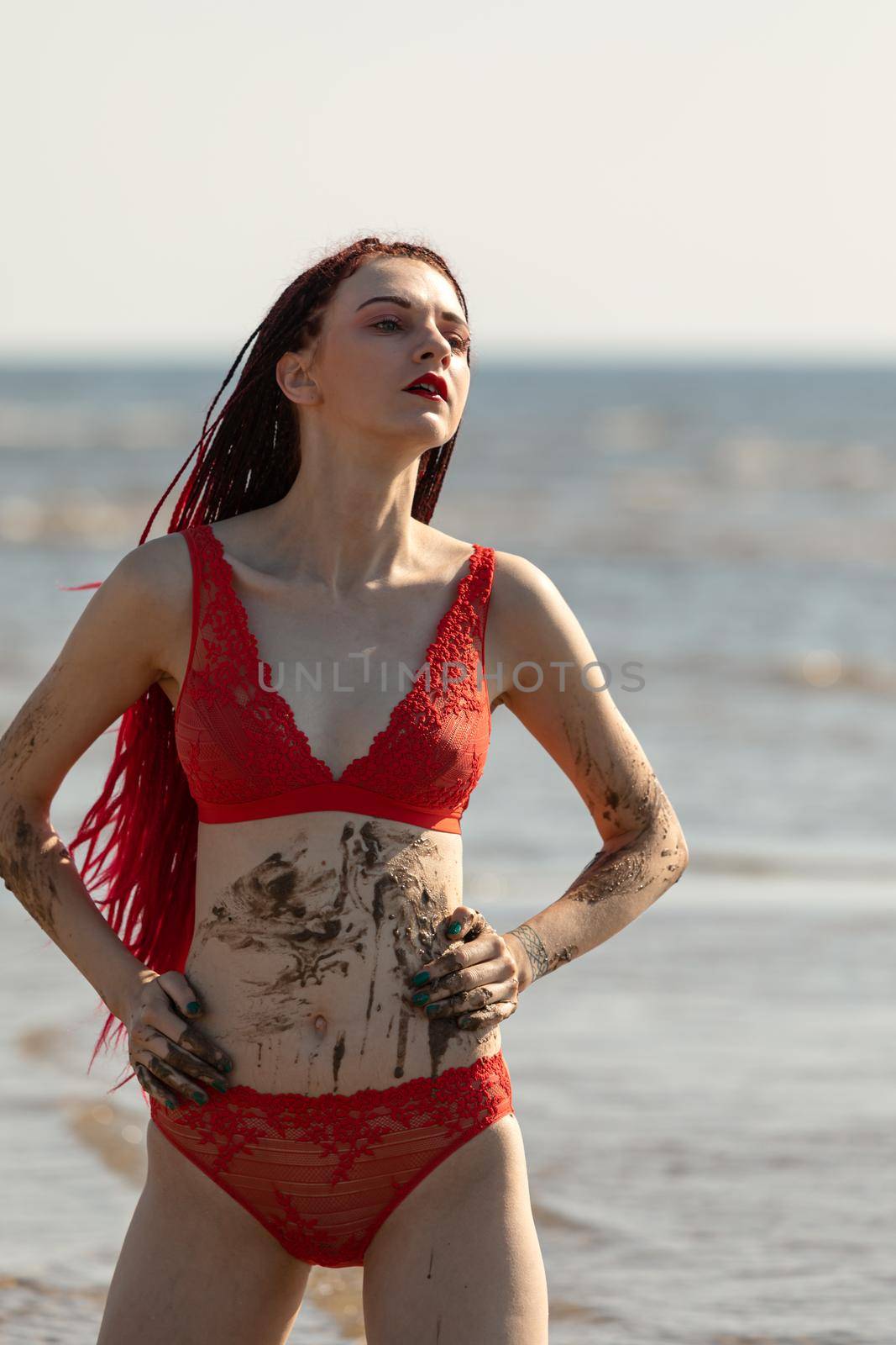 Beautiful girl outdoors enjoying nature. Seminude girl with scarlet dreadlocks in a red bathing suit sunbathes on the beach