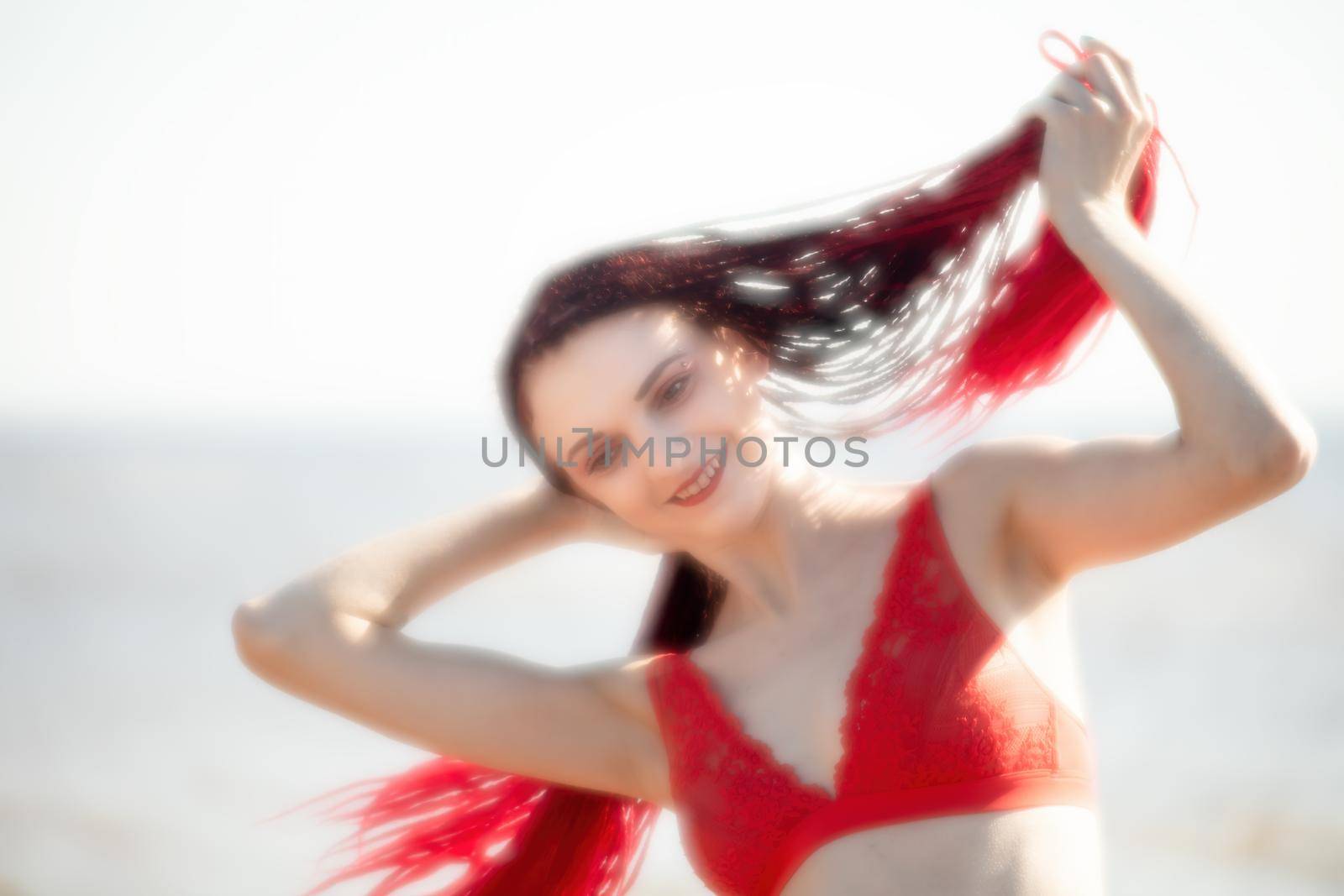 Soft focus blurred image of a beautiful young woman with scarlet dreadlocks and red bathing suit enjoying nature on the beach