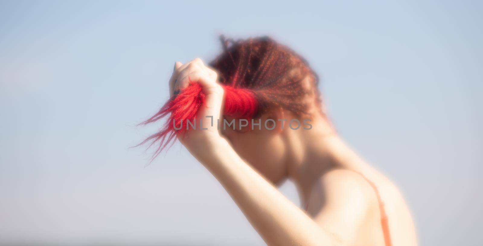 Soft focus blurred image of a beautiful young woman with scarlet dreadlocks and red bathing suit enjoying nature on the beach
