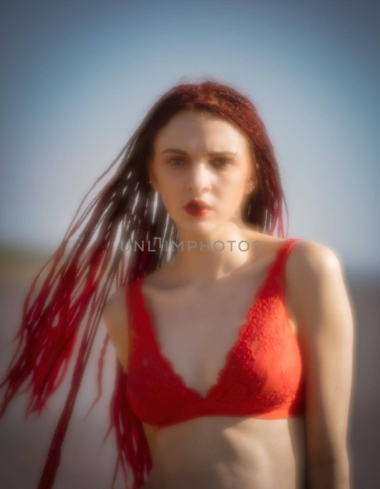 Soft focus blurred image of a beautiful young woman with scarlet dreadlocks and red bathing suit enjoying nature on the beach