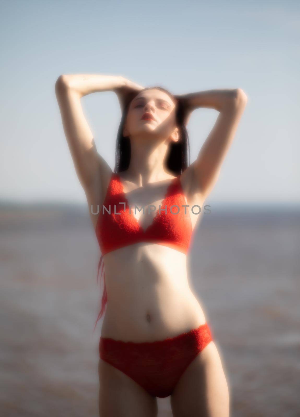 Soft focus blurred image of a beautiful young woman with scarlet dreadlocks and red bathing suit enjoying nature on the beach