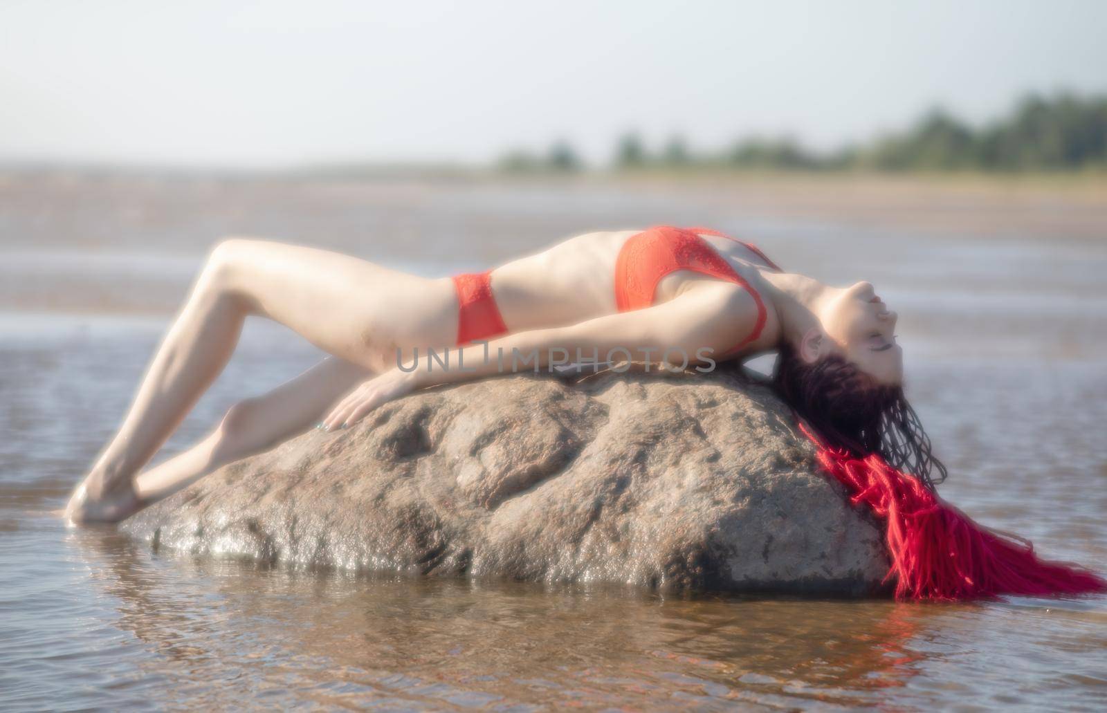 Soft focus blurred image of a beautiful young woman with scarlet dreadlocks and red bathing suit enjoying nature on the beach