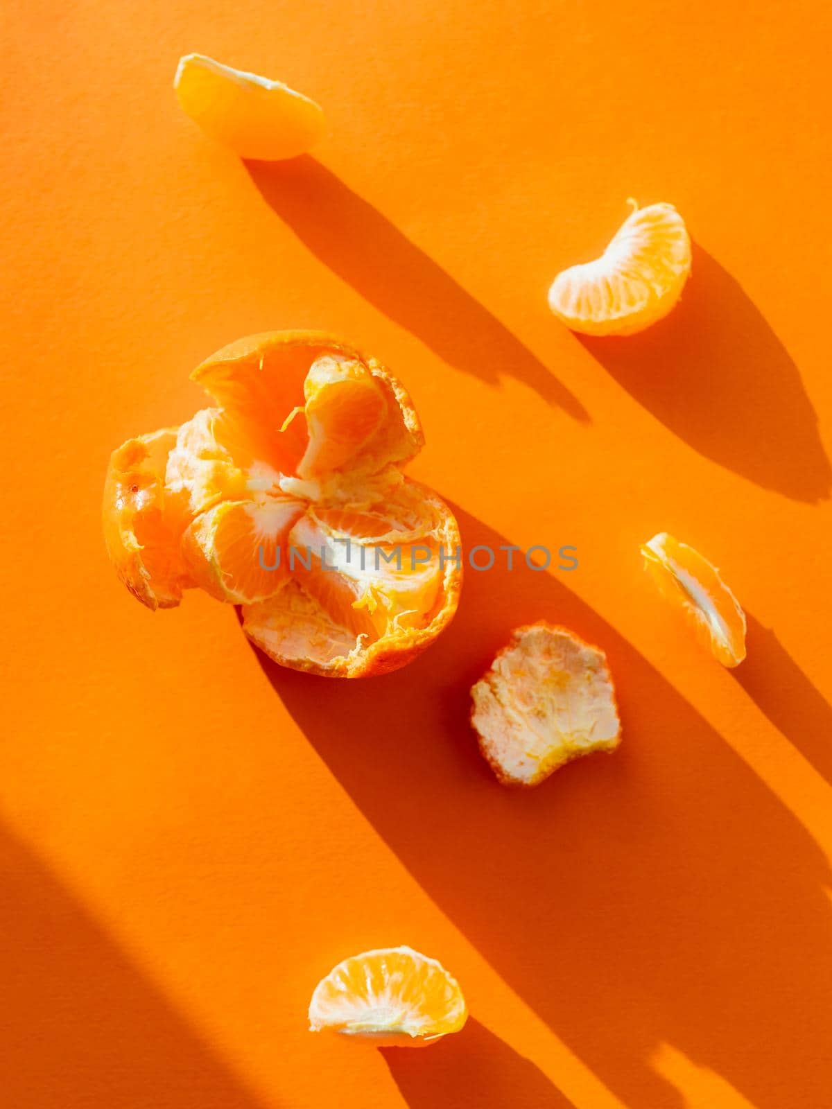 Top view of a peeled tangerine. Peel and pieces of citrus on bright orange background. Ripe fruit on sunlight. by aksenovko