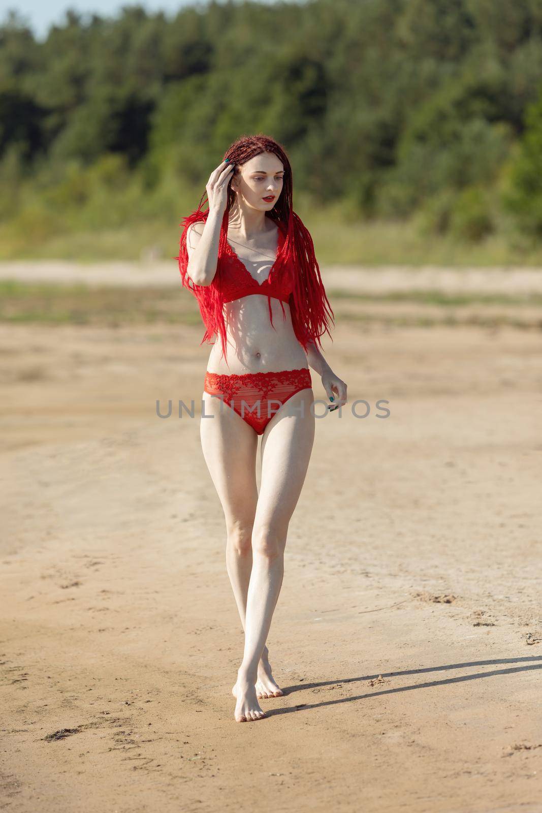 Beautiful young woman with scarlet dreadlocks and red bathing suit enjoying nature. 