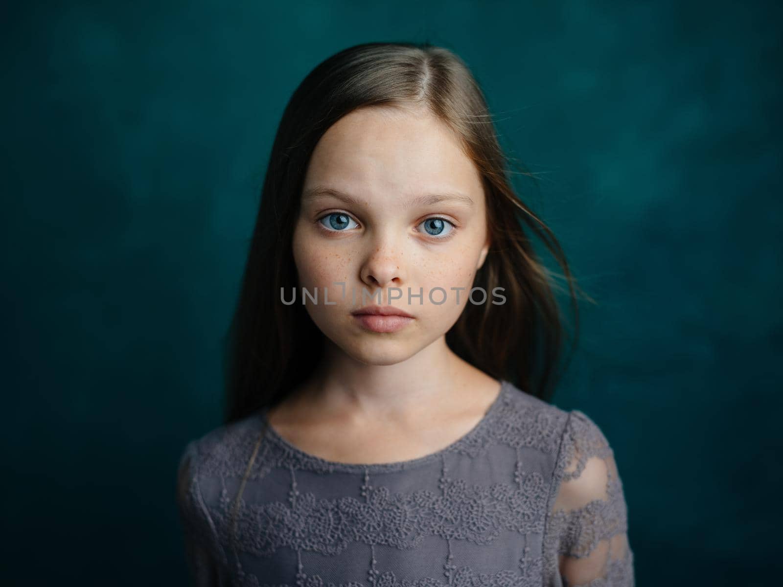 Cute blue-eyed girl in a gray dress on a green background cropped view. High quality photo