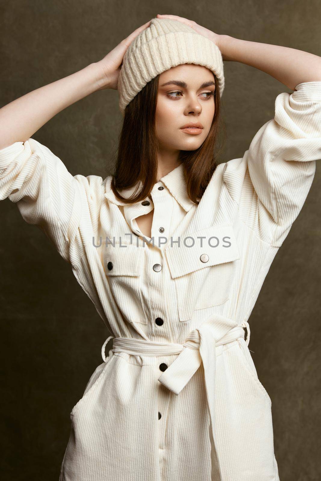 fashionable brunette in a hat and jumpsuit hold her hands behind her head on a brown background by SHOTPRIME