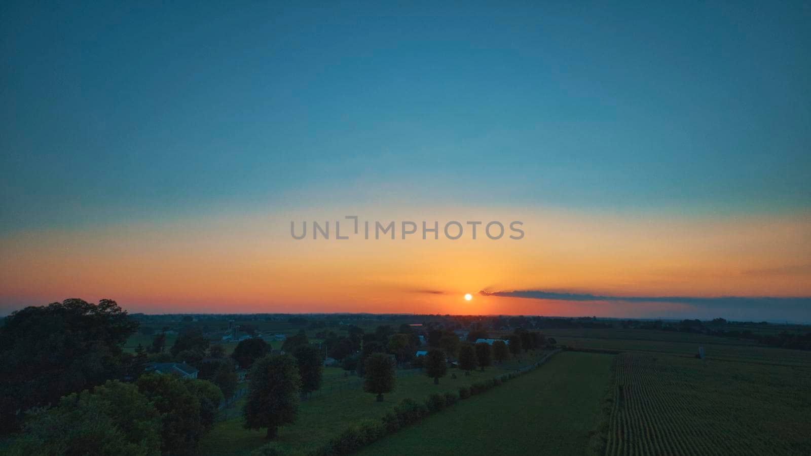An Aerial View of a Sunset over Green Farm Lands with a Reddish Sky