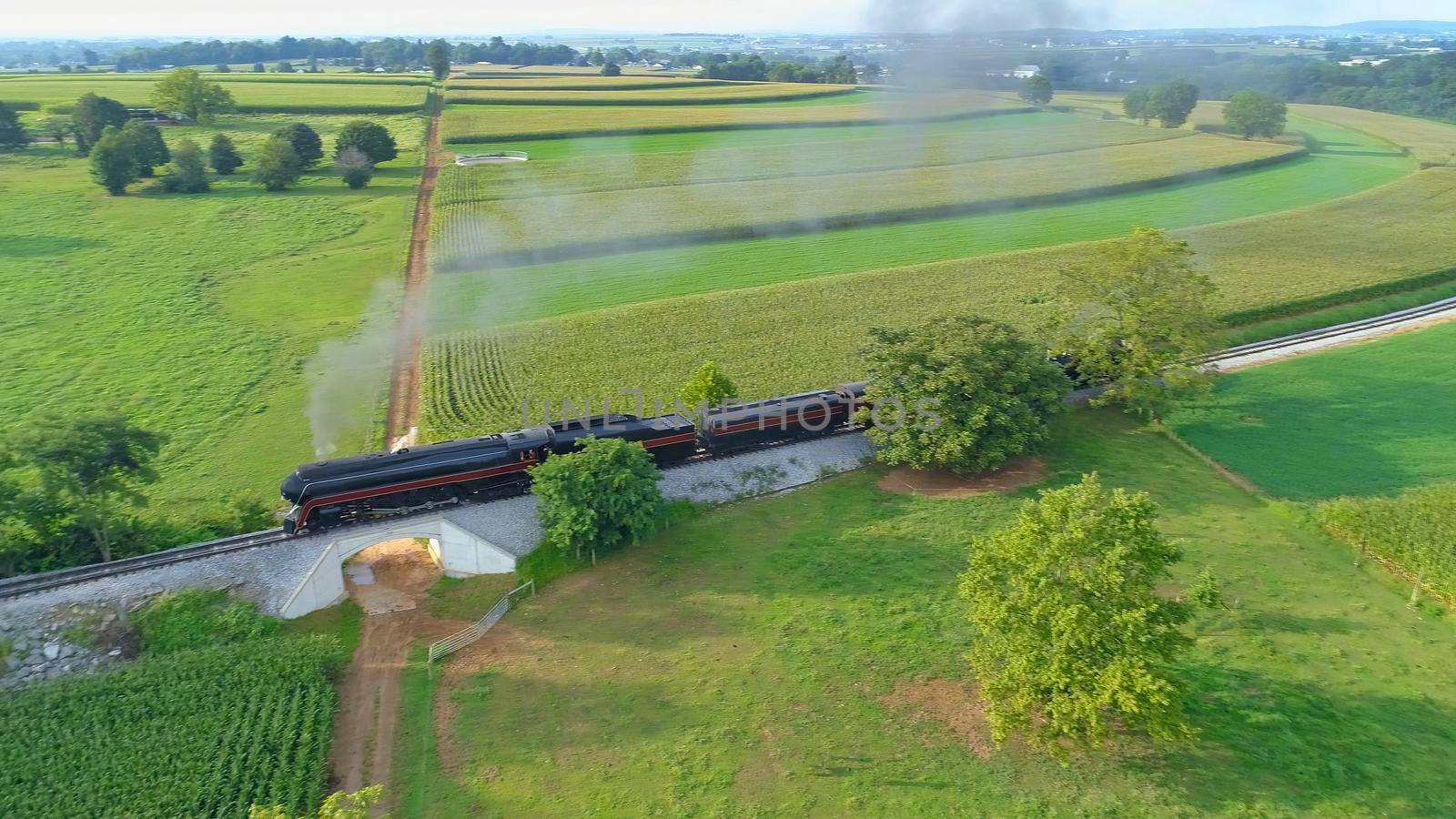 Aerial View of An Antique Restored Steam Locomotive Blowing Smoke and Steam Traveling Thru Farmlands and Countryside on a Sunny Summer Day