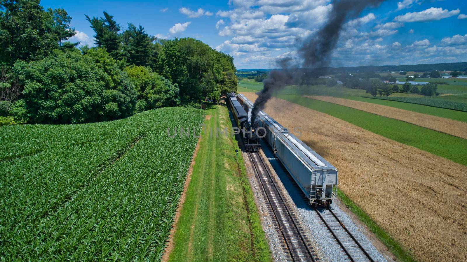 Aerial View of An Antique Restored Steam Locomotive Blowing Smoke and Steam Traveling Thru Farmlands and Countryside on a Sunny Summer Day