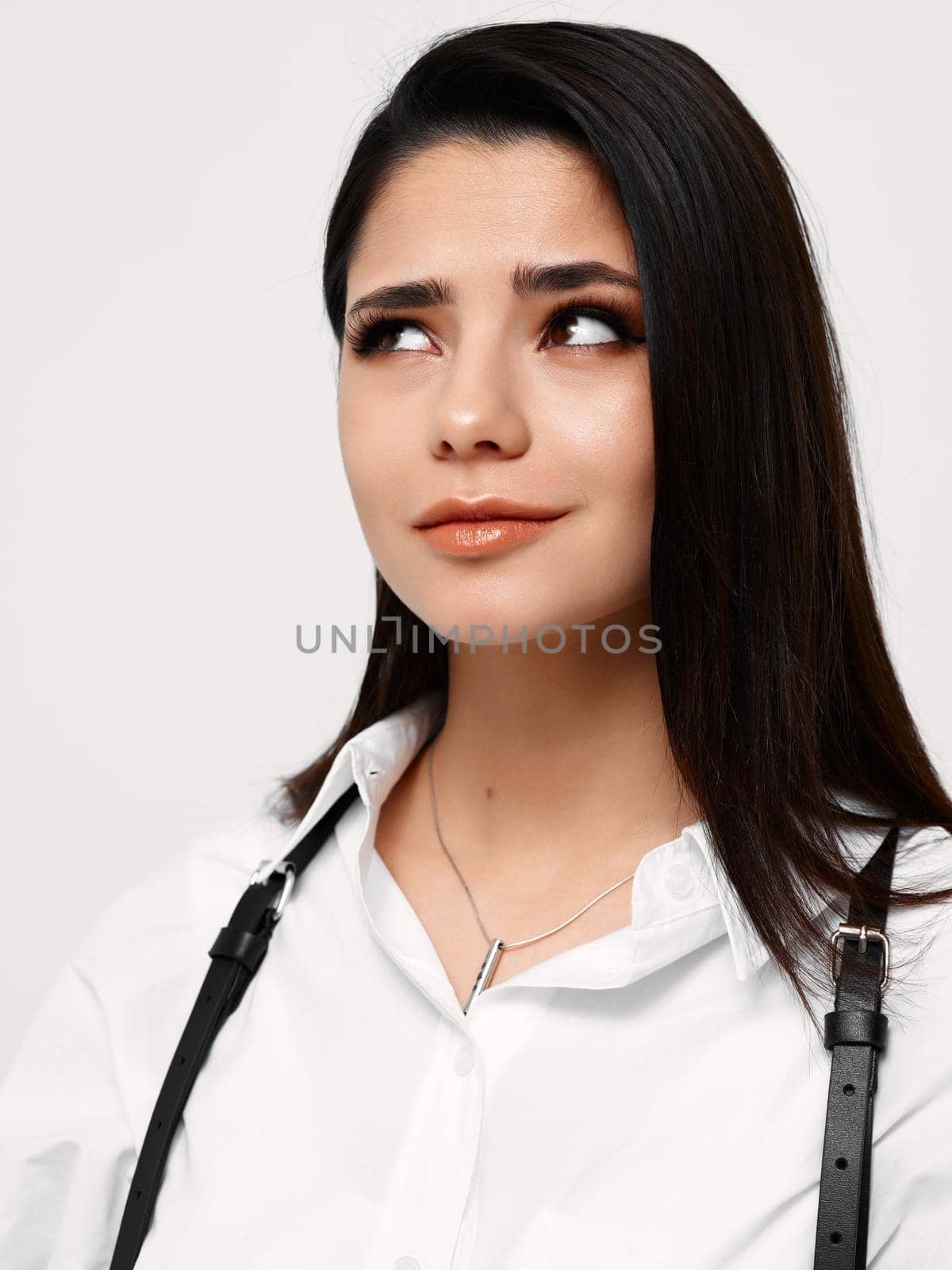 confident brunette woman in white shirt looking to the side on light background. High quality photo