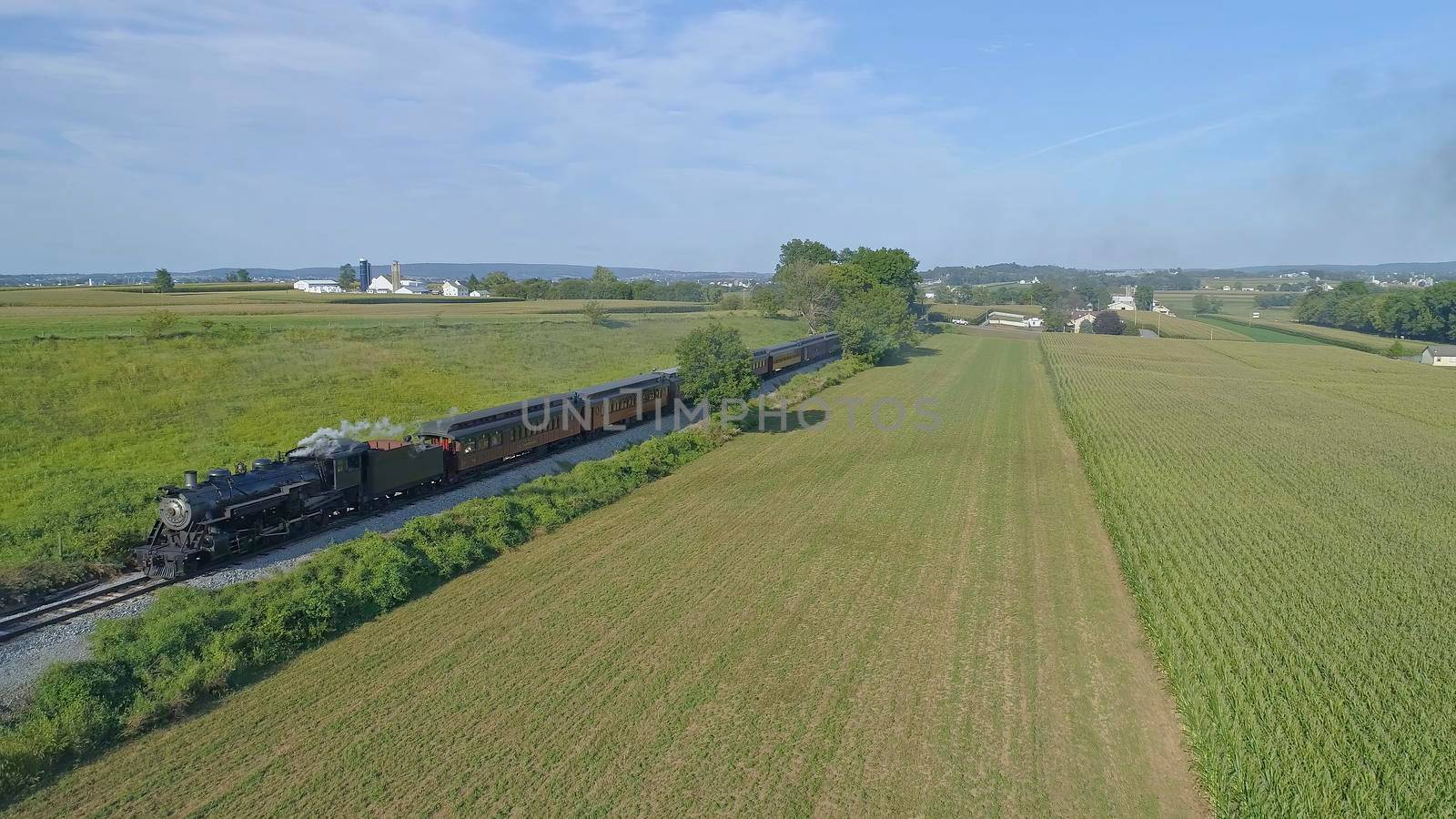 Aerial View of An Antique Restored Steam Locomotive Blowing Smoke and Steam Traveling Thru Farmlands and Countryside on a Sunny Summer Day