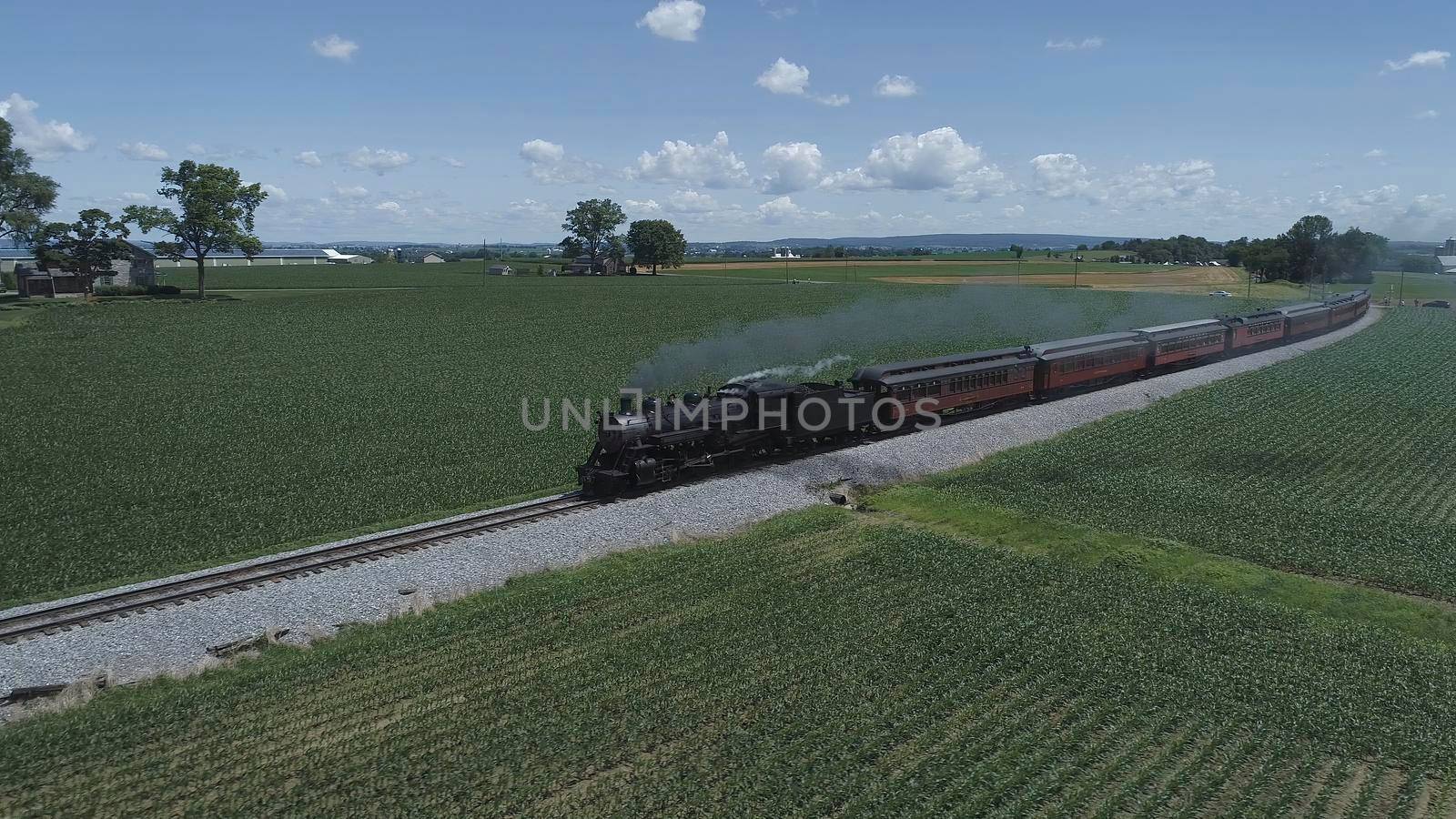 Aerial View of An Antique Restored Steam Locomotive Blowing Smoke and Steam Traveling Thru Farmlands and Countryside on a Sunny Summer Day