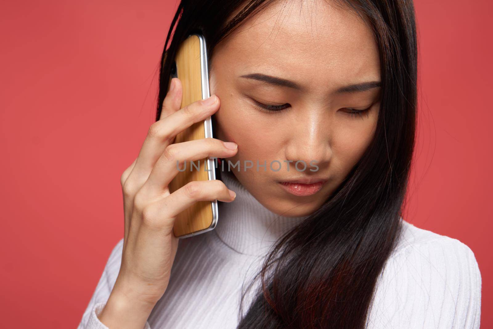 sad asian woman talking on the phone close-up red background by SHOTPRIME