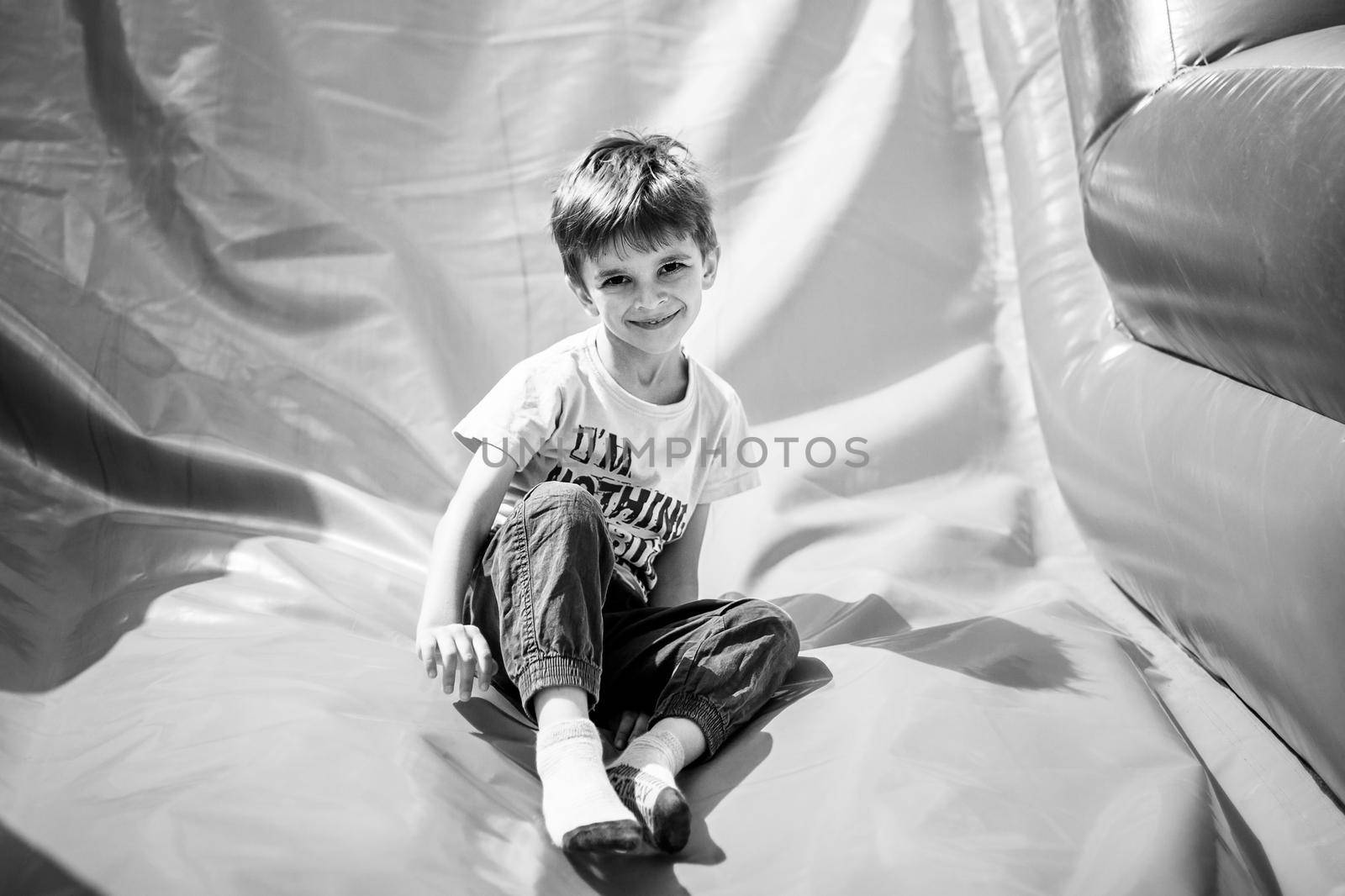 Smiling little boy playing on inflatable slide, looking at camera, black and white shot