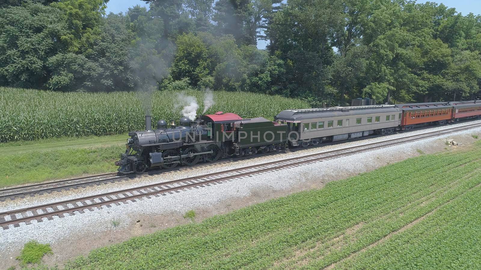 Aerial View of An Antique Restored Steam Locomotive Blowing Smoke and Steam Traveling Thru Farmlands and Countryside on a Sunny Summer Day