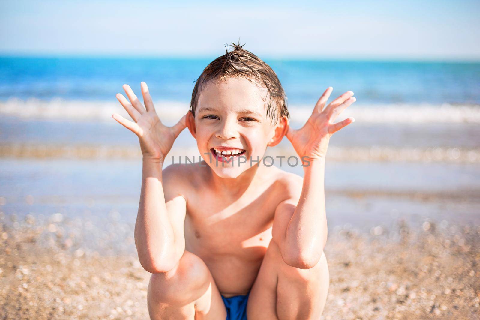smiling boy with hands close to the head sitting on the beach