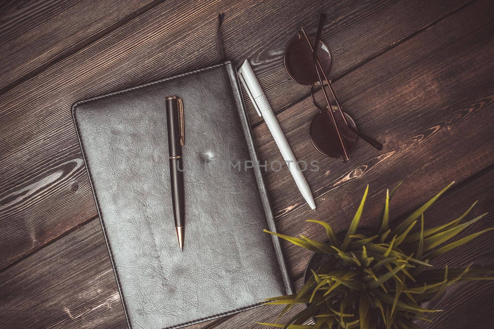 book with black cover and lies on a wooden table and a pen pencil jobs glasses flower potted coffee cup by SHOTPRIME
