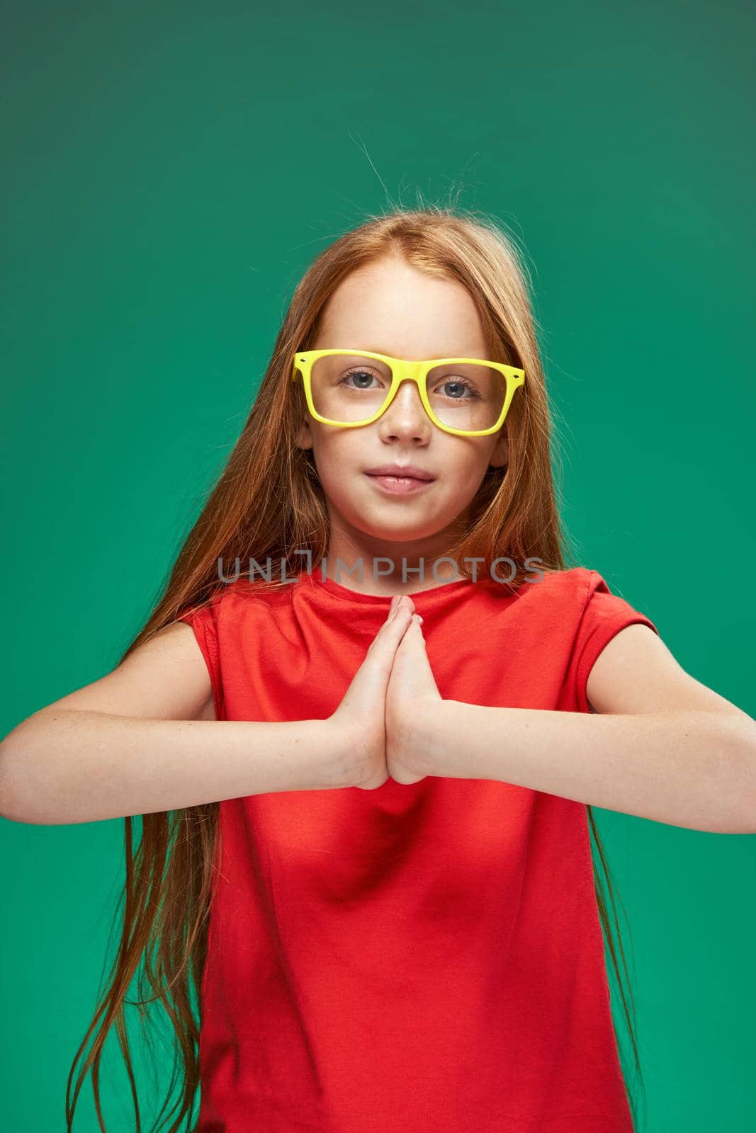 redhead girl with yellow glasses gesturing with her hands childhood learning Green background. High quality photo