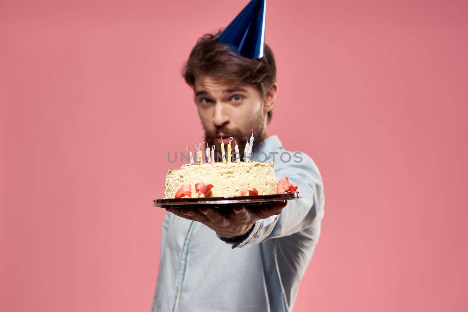 Man with cake in a plate and in a blue shirt on a pink background birthday holidays cropped view. High quality photo