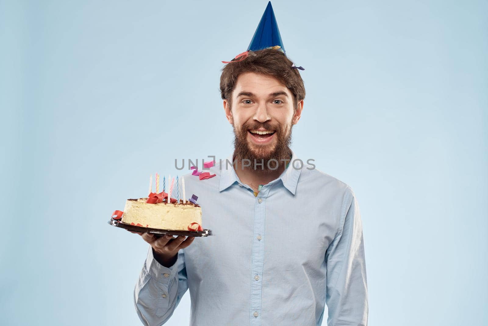Man with a plate of cake and a festive candle blue background cap corporate party. High quality photo