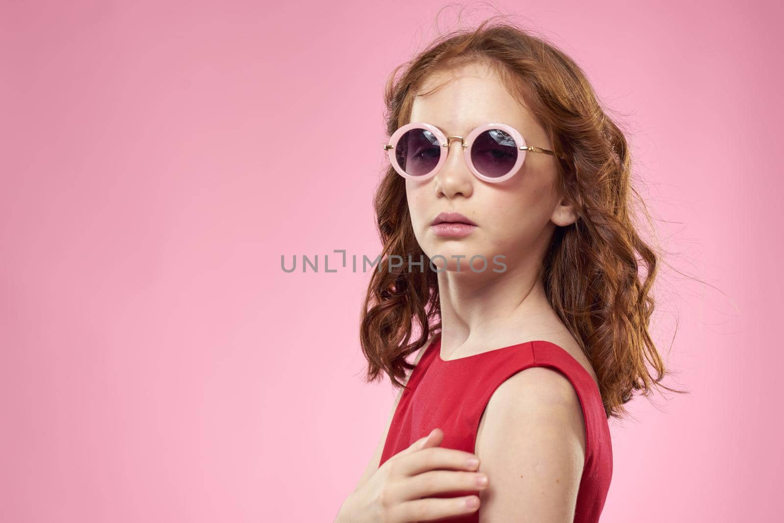 Cheerful little girl childhood dark glasses red dress lifestyle pink background. High quality photo