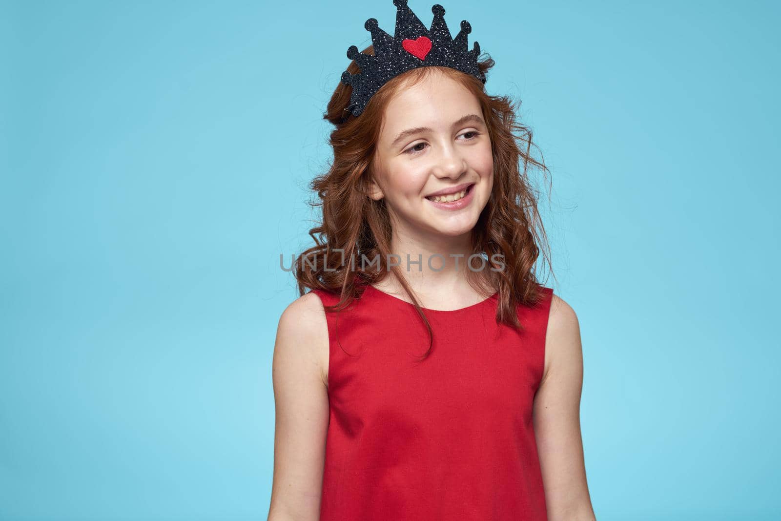 Girl with curly hair with a crown on her head red dress lifestyle blue background. High quality photo