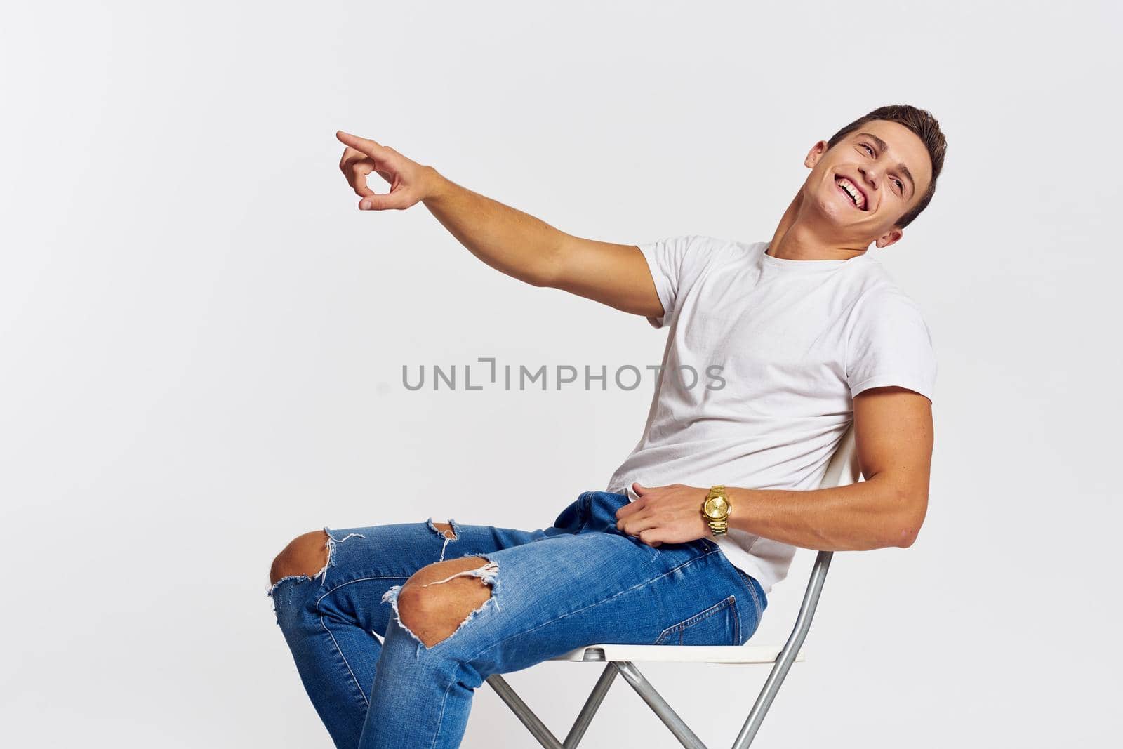 Man on a chair indoors torn jeans white t-shirt handsome face model light background. High quality photo