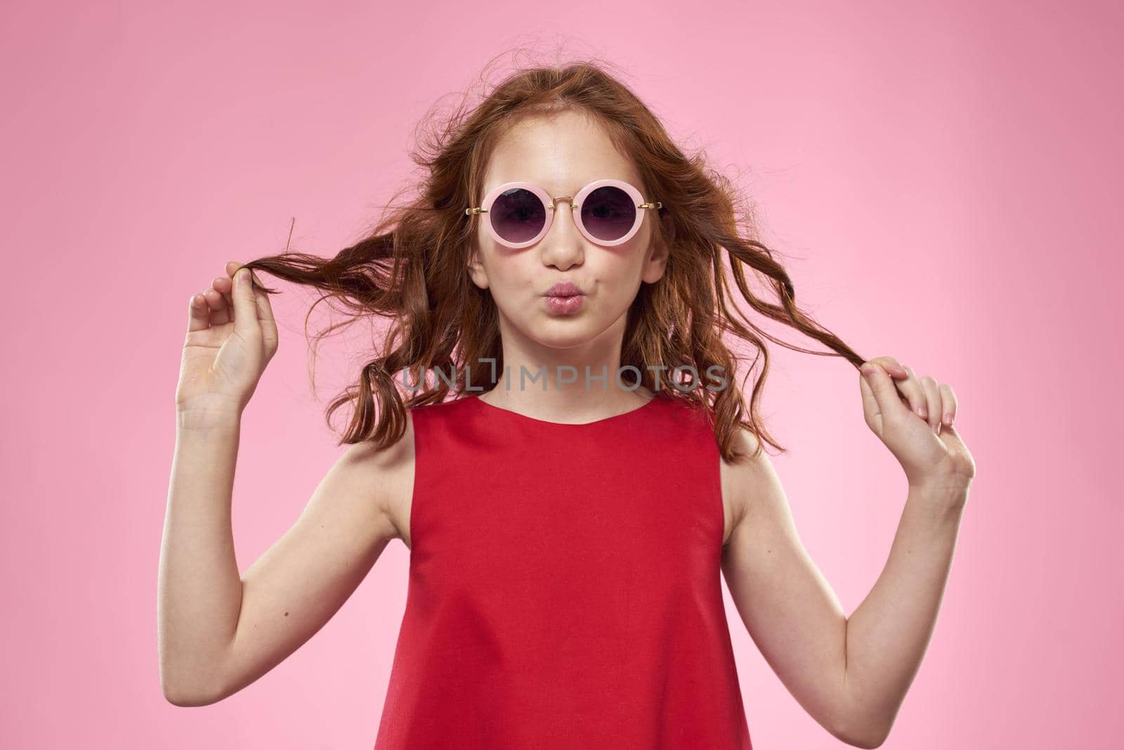 Cheerful little girl childhood dark glasses red dress lifestyle pink background. High quality photo