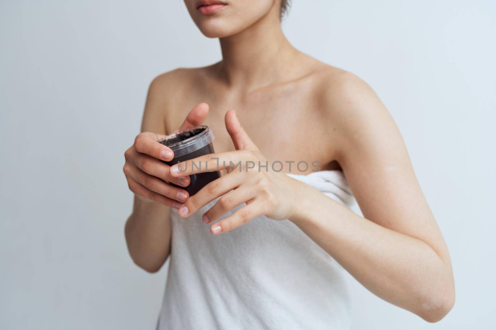Woman in towel bared shoulders black cream in clean skin hands. High quality photo