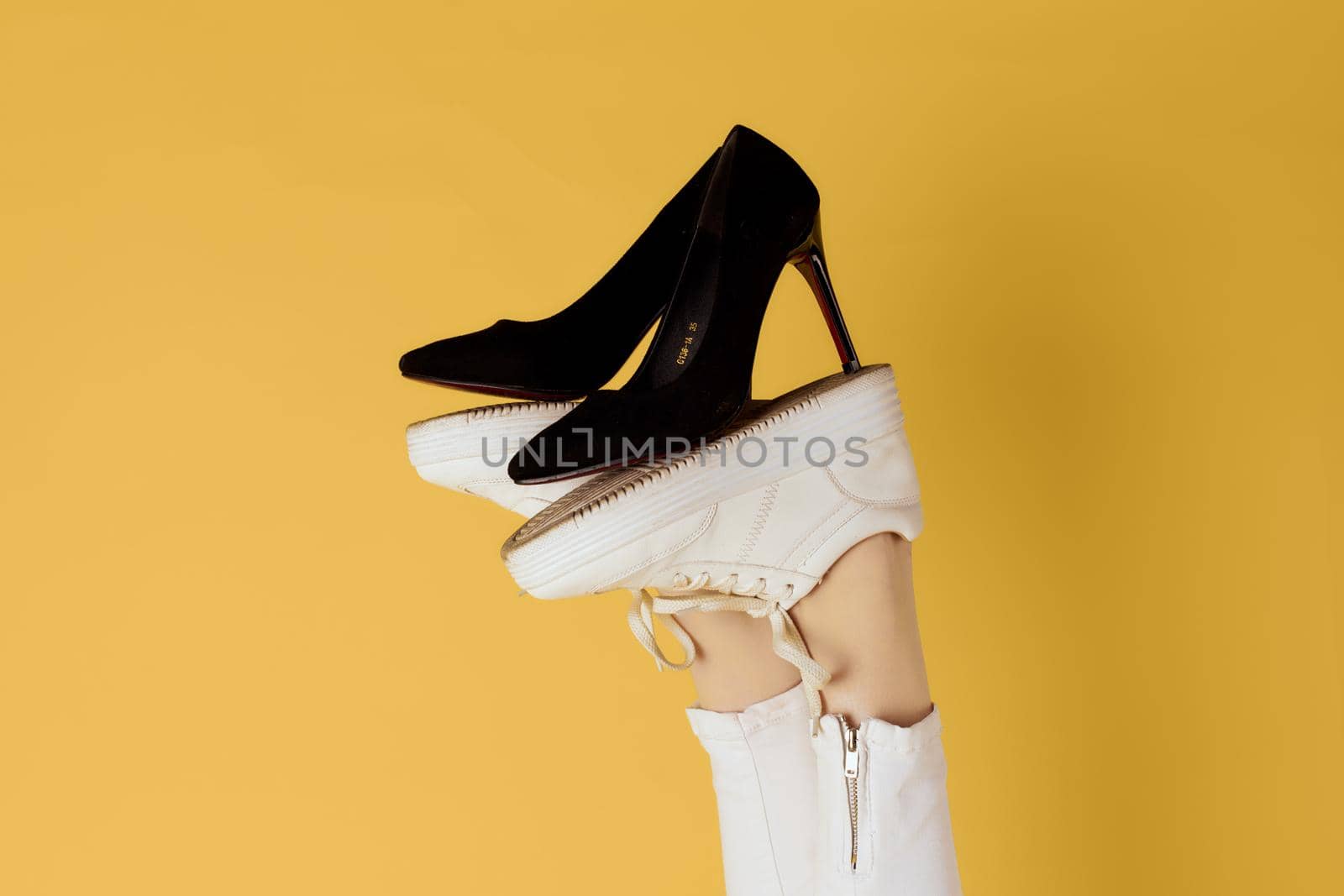 Female feet in sneakers black fashion shoes yellow background by SHOTPRIME