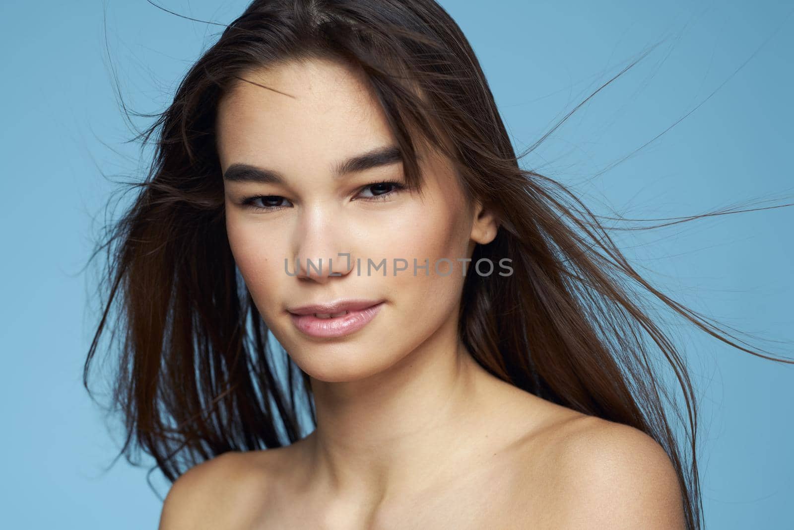 pretty brunette naked shoulders long hair skin care blue background. High quality photo