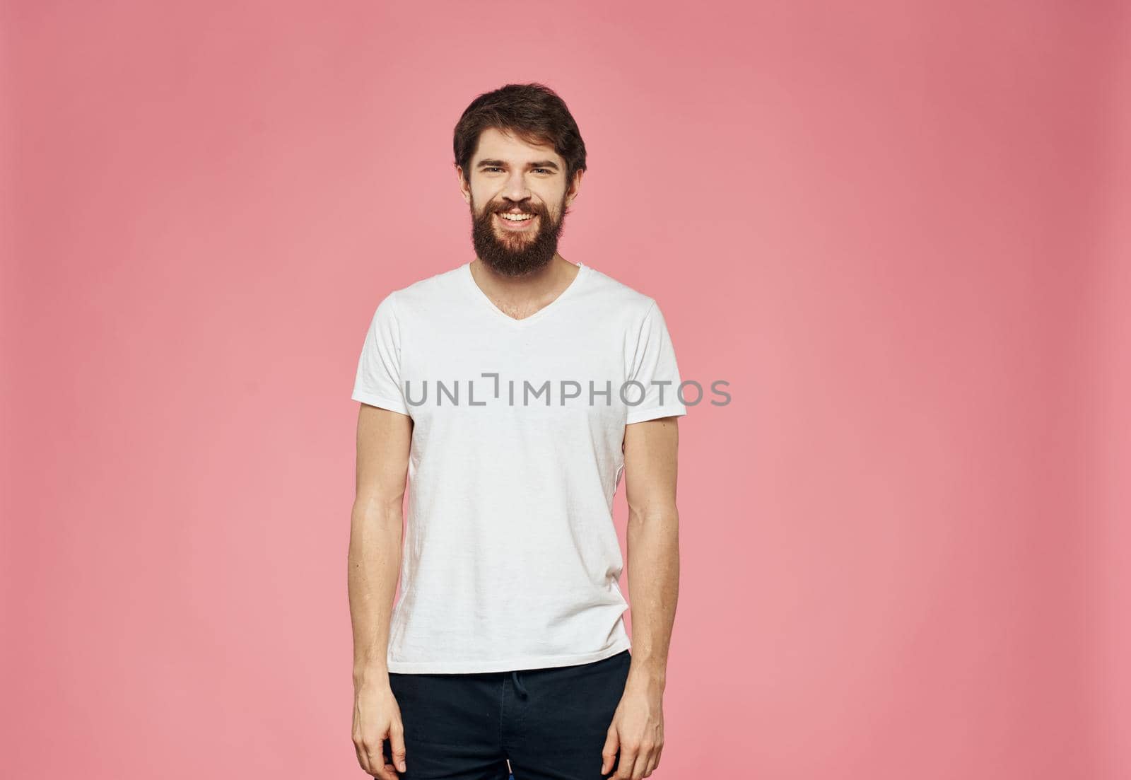 Bearded guy in a T-shirt and trousers on a pink background. High quality photo
