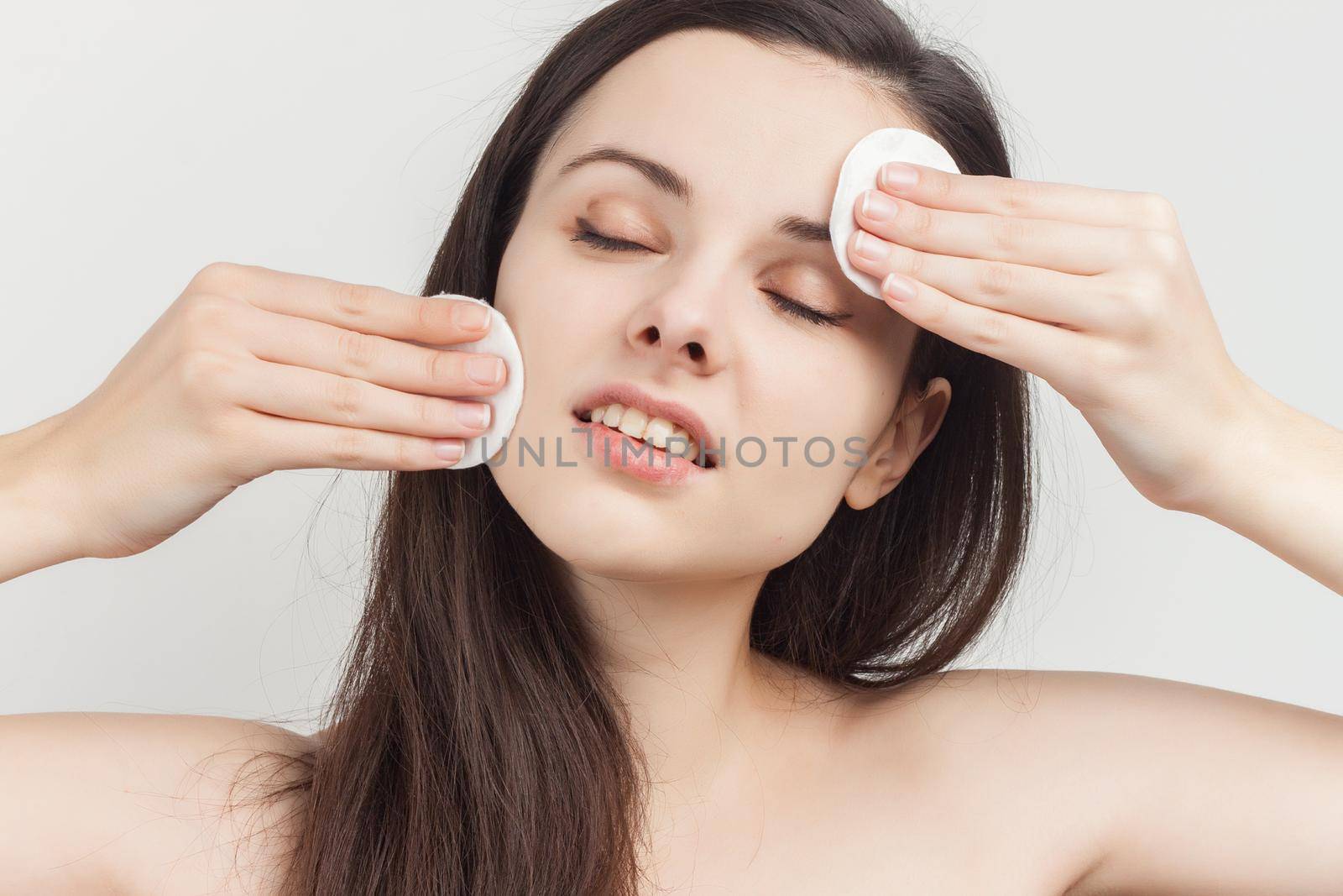pretty brunette naked shoulders wipes her face but clean skin with a sponge. High quality photo