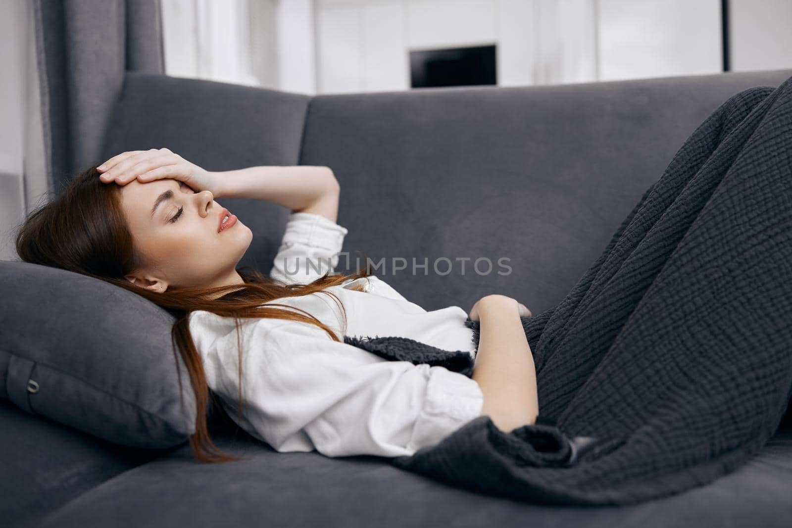 woman covered with a blanket lies on the sofa hand on her head feeling unwell. High quality photo