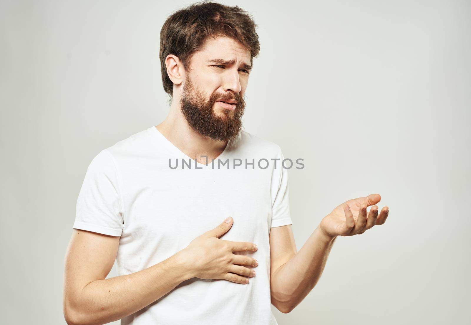 A man in a white T-shirt gestures with his hands on a light background cropped view of the emotion model. High quality photo
