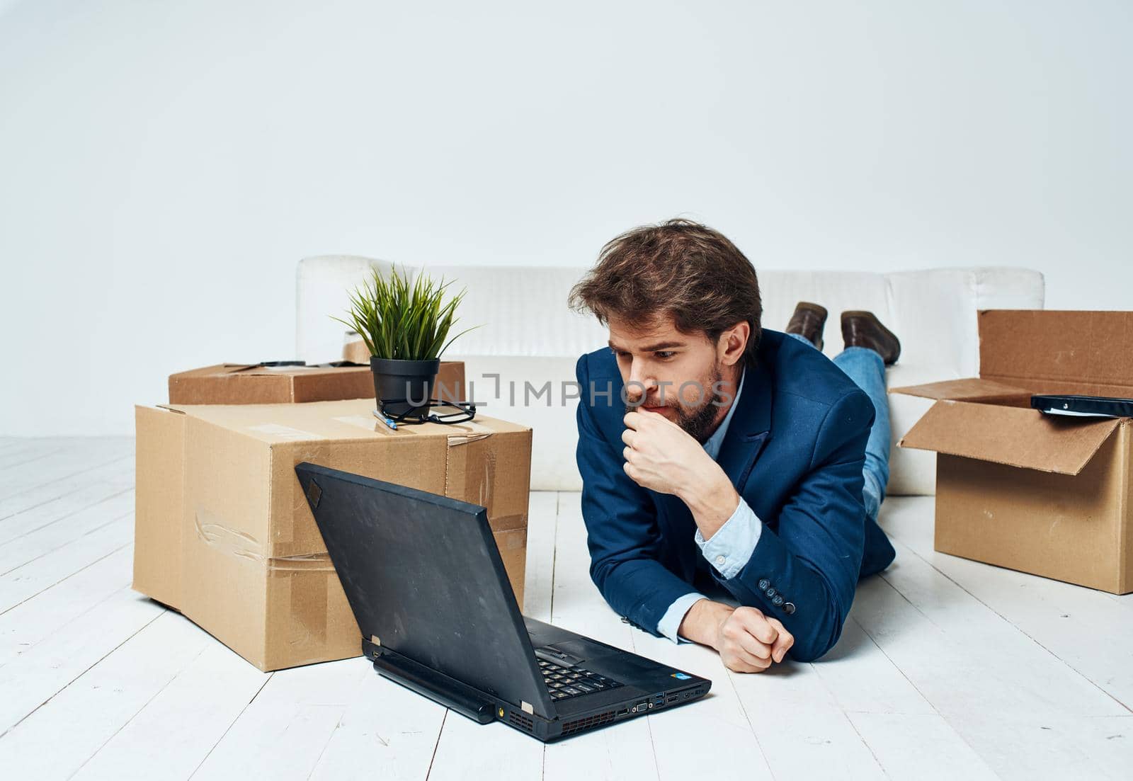 A business man lies on the floor in front of a laptop, work with no unpacked things. High quality photo