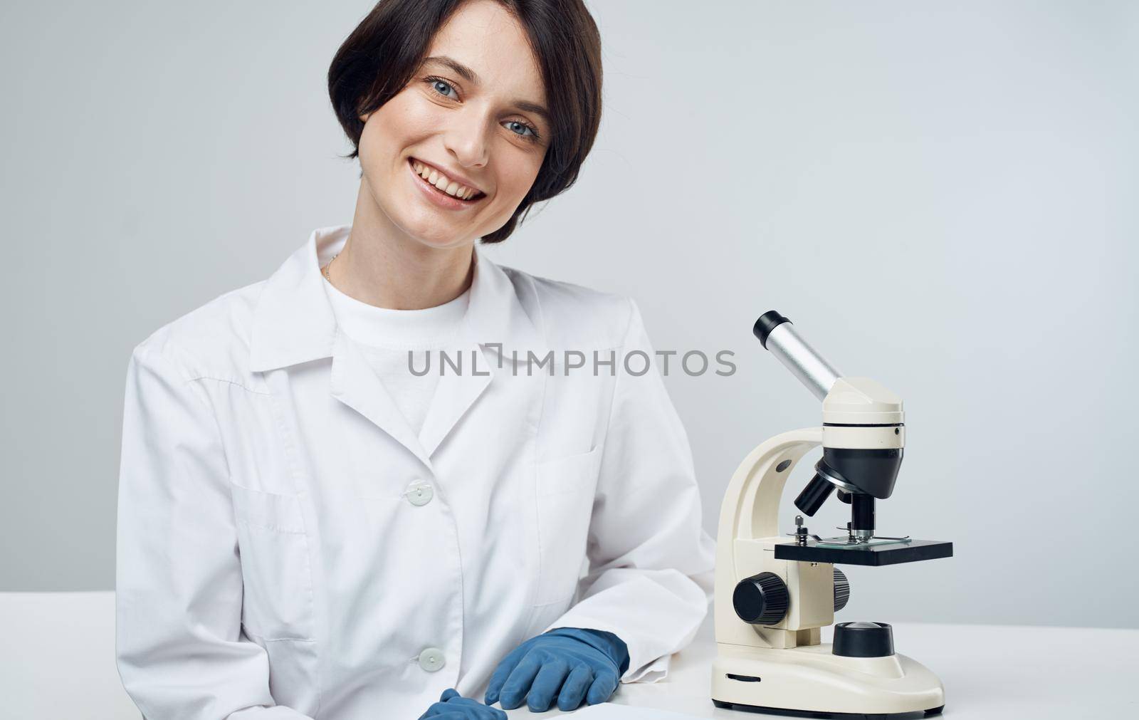 woman doctor in a medical gown with a microscope on the table sits on a chair in a bright room. High quality photo