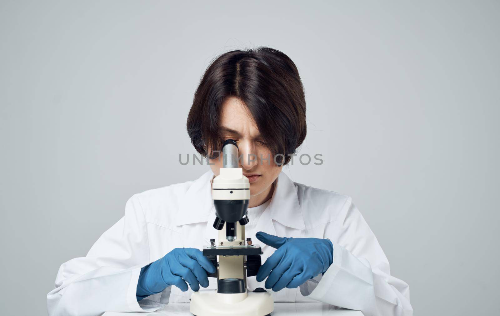 woman doctor in a medical gown with a microscope on the table sits on a chair in a bright room by SHOTPRIME