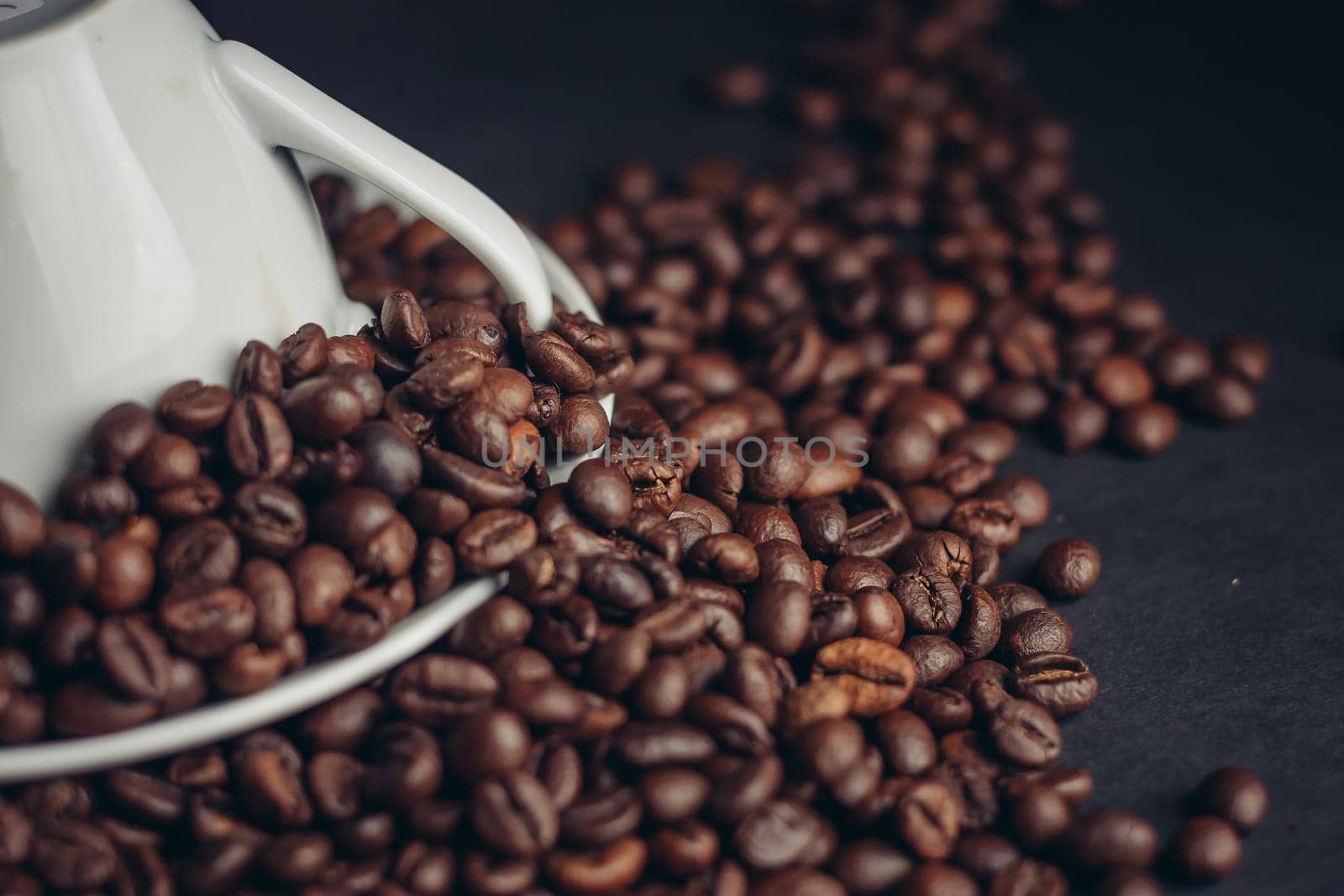white cup and saucer and large coffee beans on a dark background macro photography. High quality photo