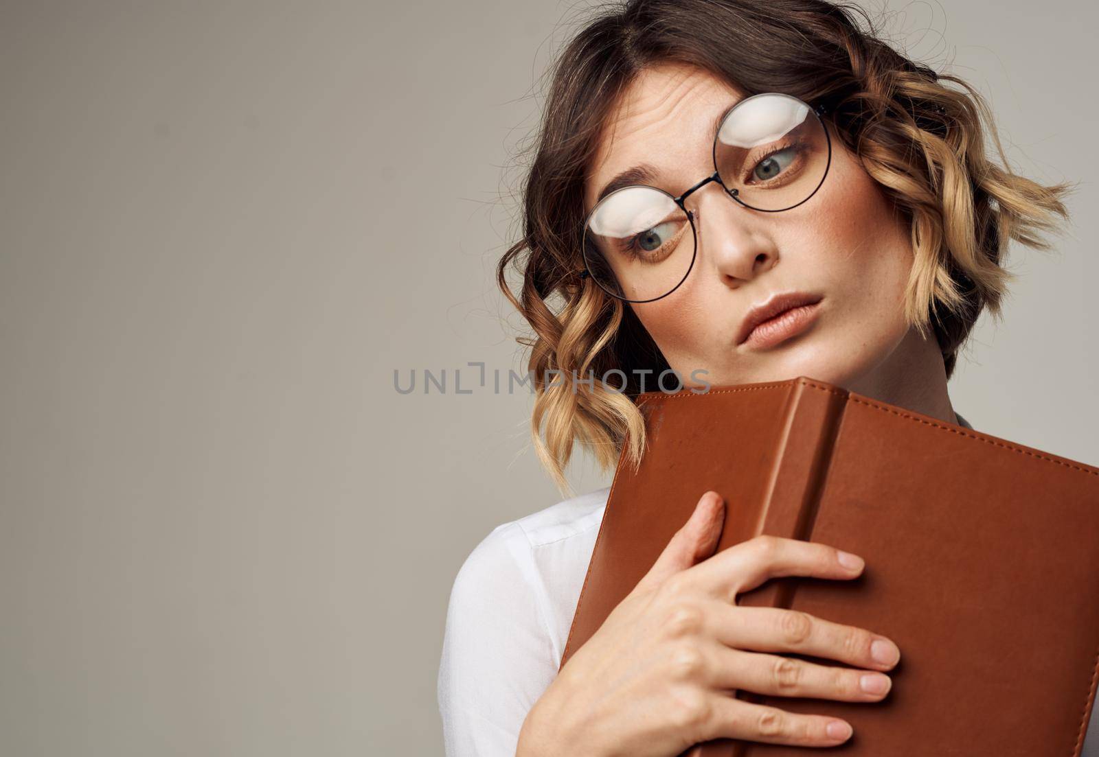 Romantic woman in glasses on a gray background with a brown book in her hands. High quality photo