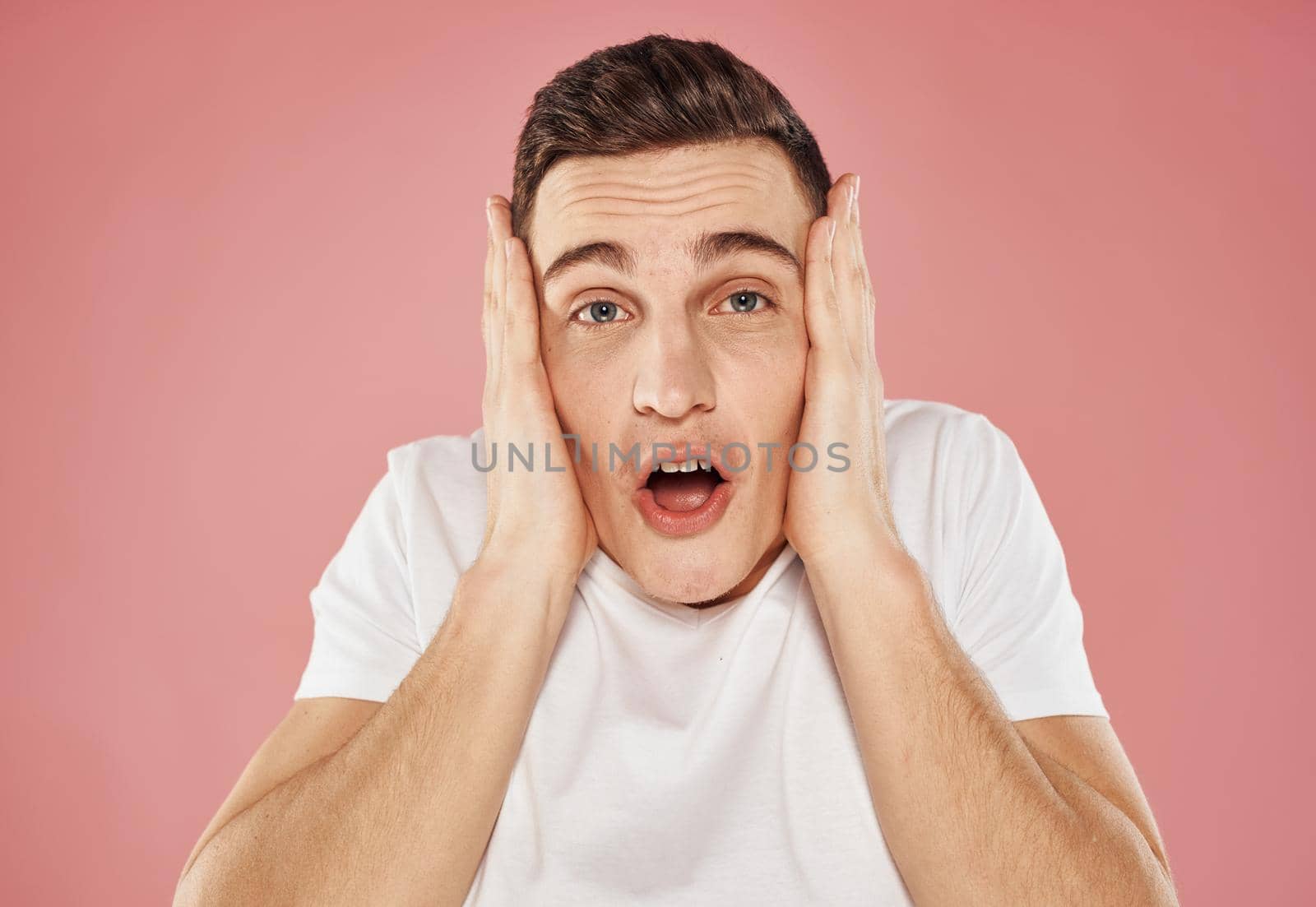 Happy man on pink background gesturing with hands in white t-shirt cropped view. High quality photo