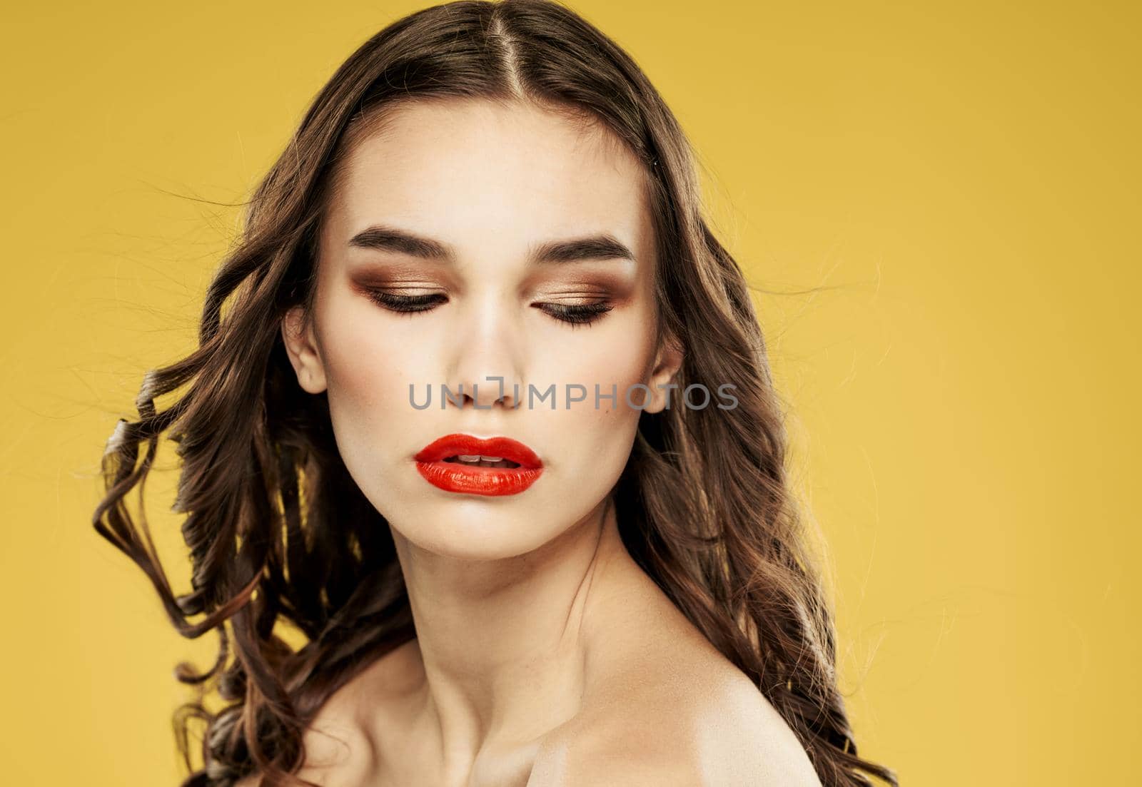 Portrait of a beautiful lady with red lips brunette eyeshadow on the eyelids yellow background by SHOTPRIME