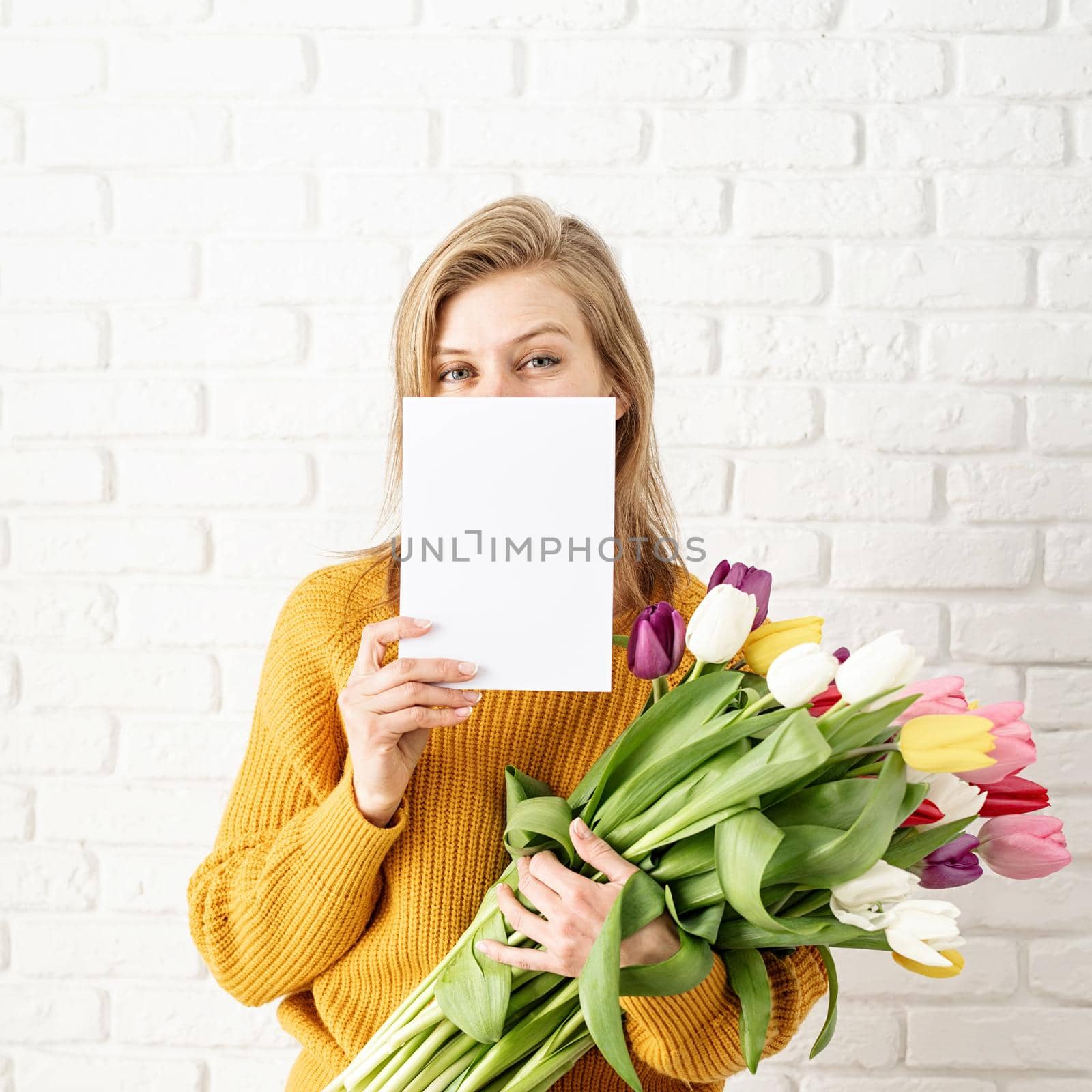 Happy beautiful woman in yellow clothes holding bouquet of tulips and blank card by Desperada