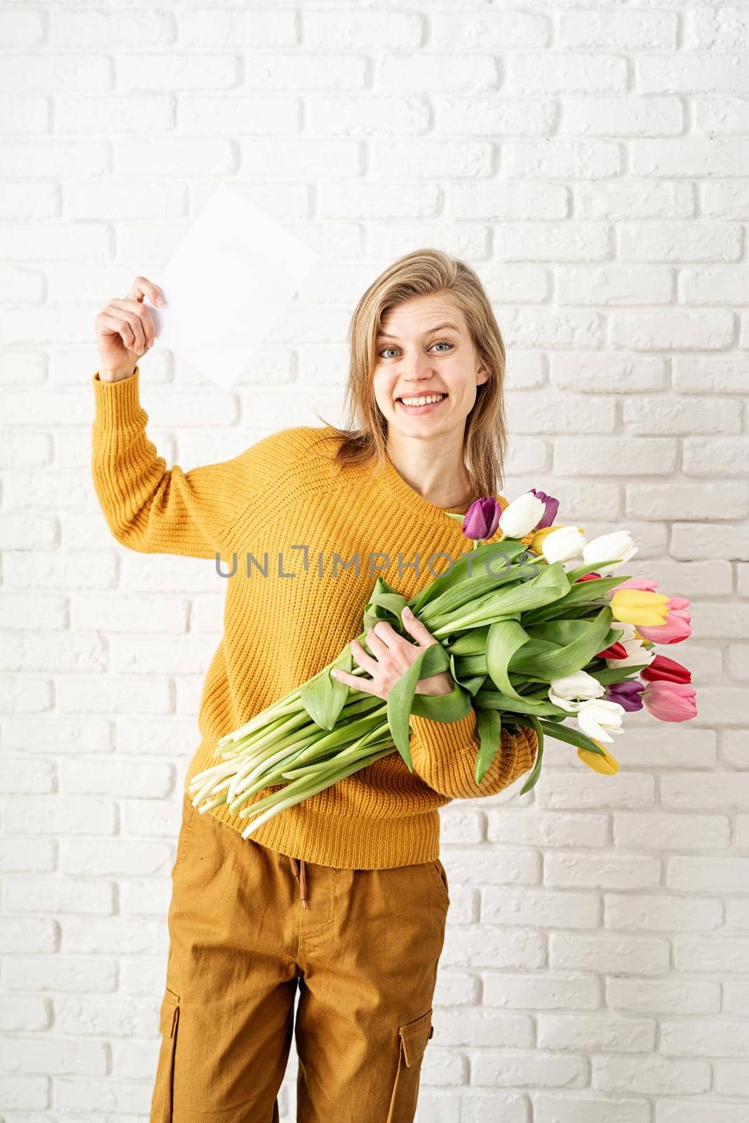 Happy beautiful woman in yellow clothes holding bouquet of tulips and blank card by Desperada