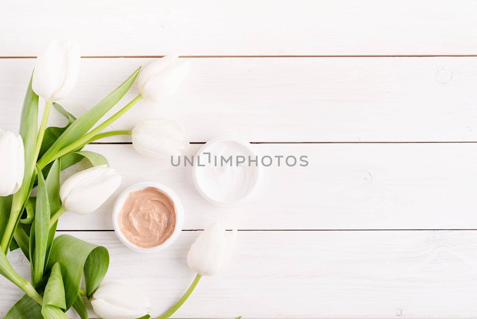 Cosmetic creams with white tulips top view flat lay on white wooden background by Desperada
