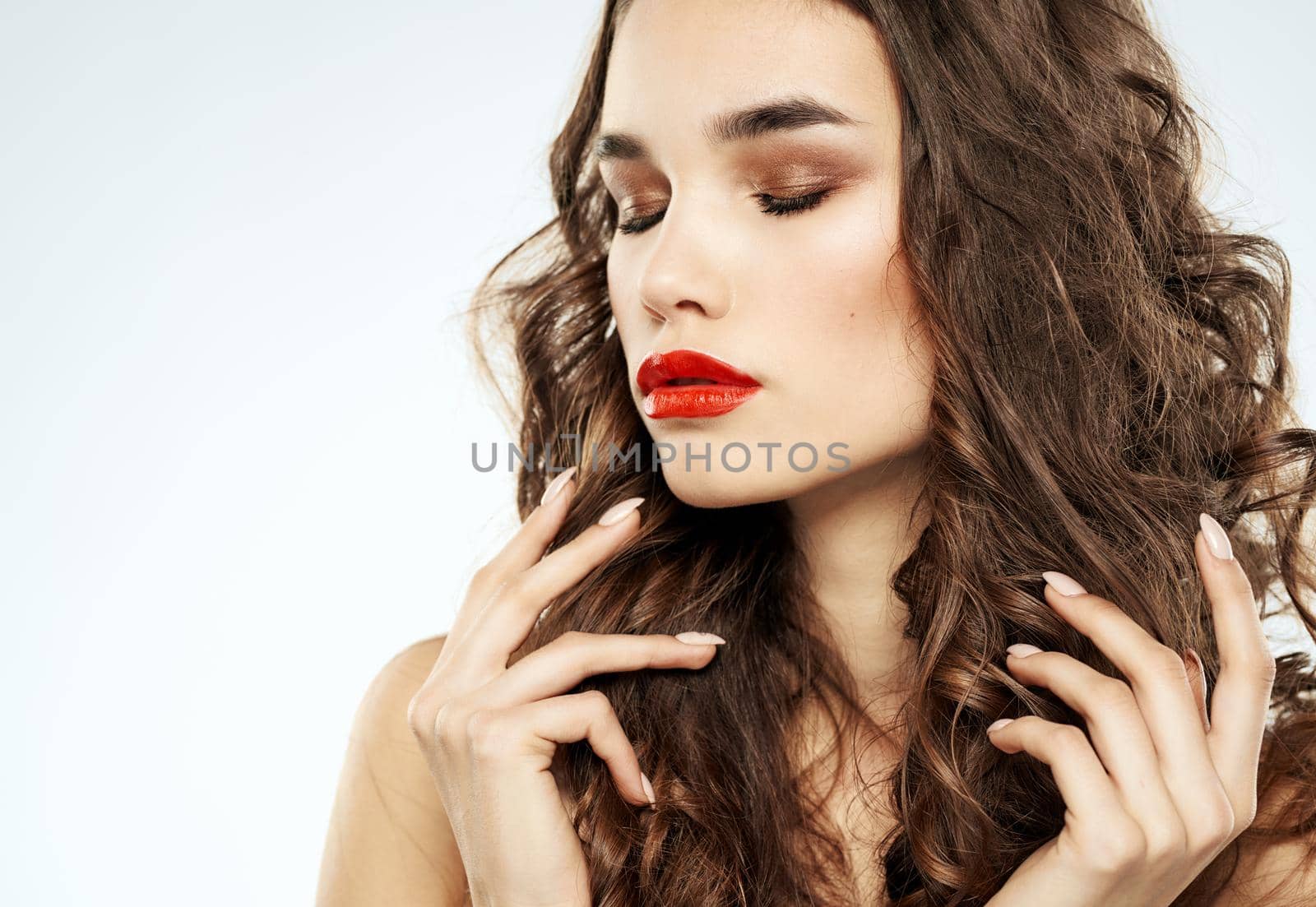 Beautiful brunette woman with bright makeup touches curly hair on her head with her hands. High quality photo