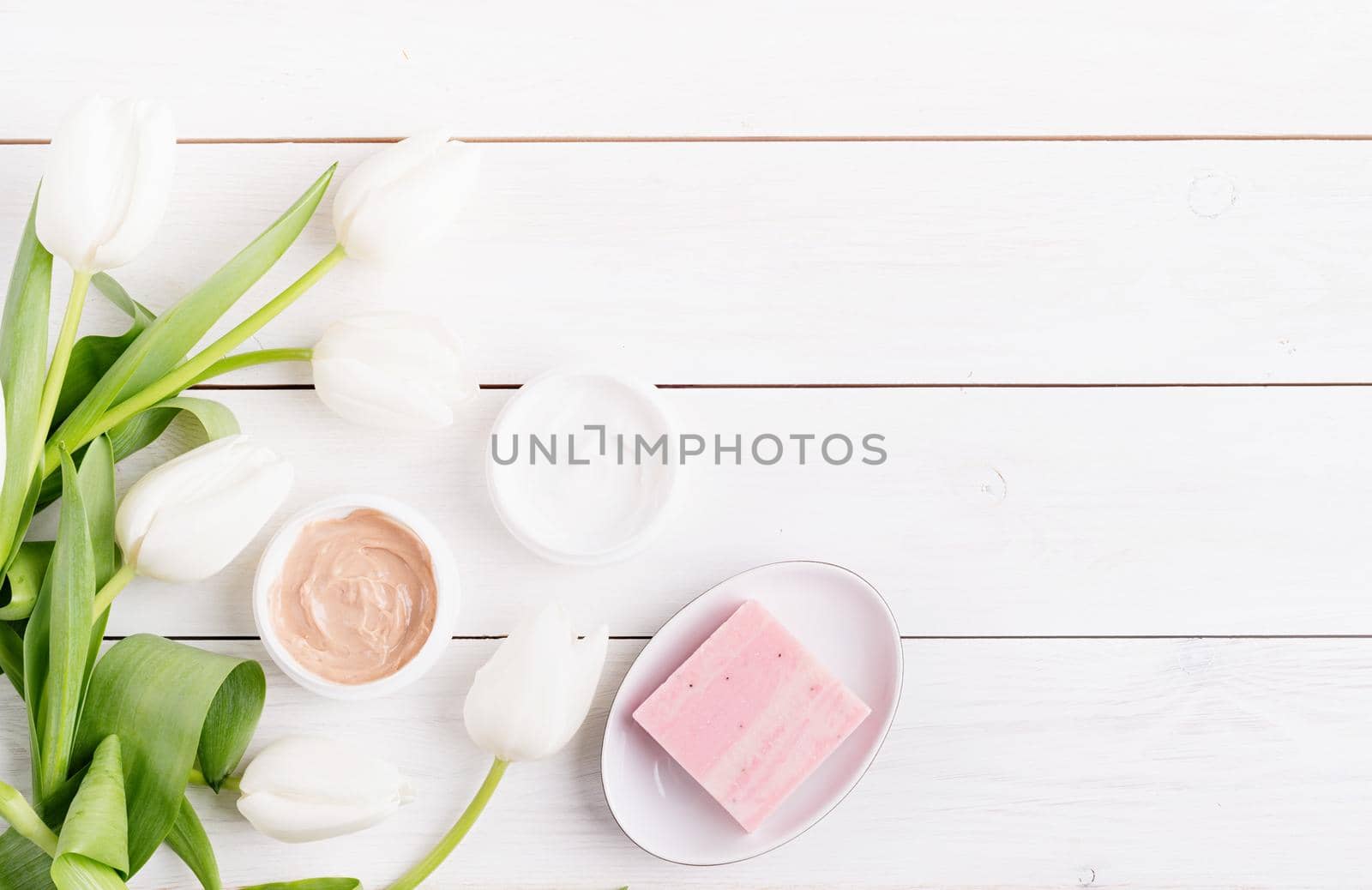Top view of cosmetic creams and soap with white tulips top view flat lay on white wooden background, flat lay