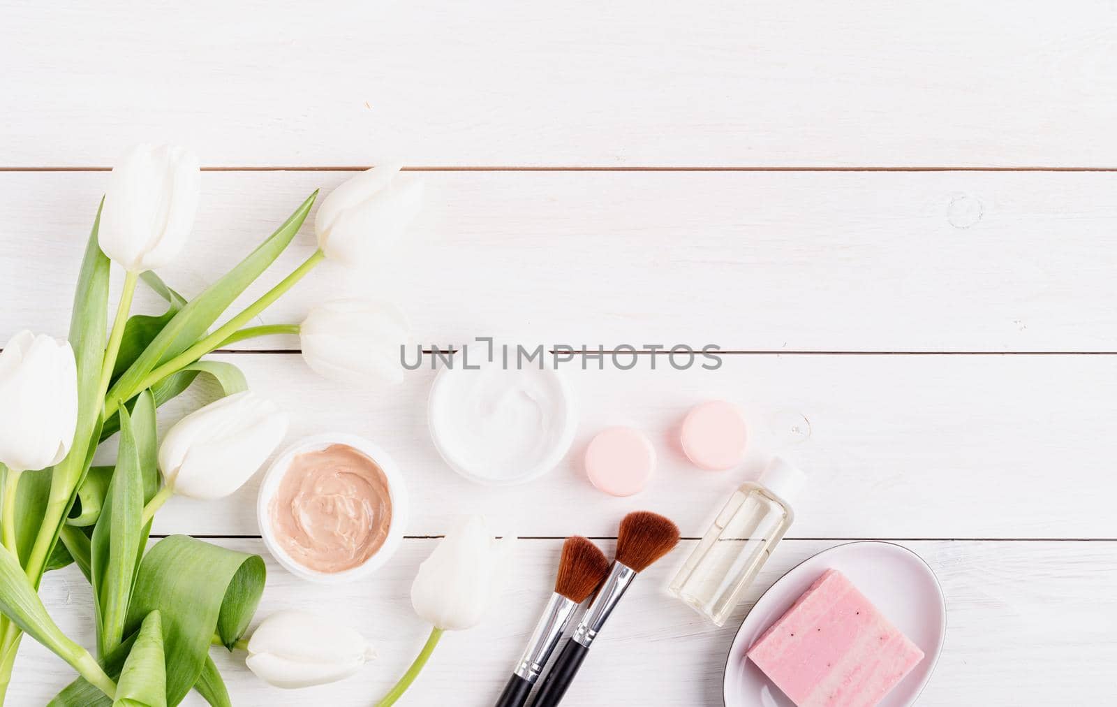 Top view of cosmetic creams and soap with white tulips top view flat lay on white wooden background, flat lay